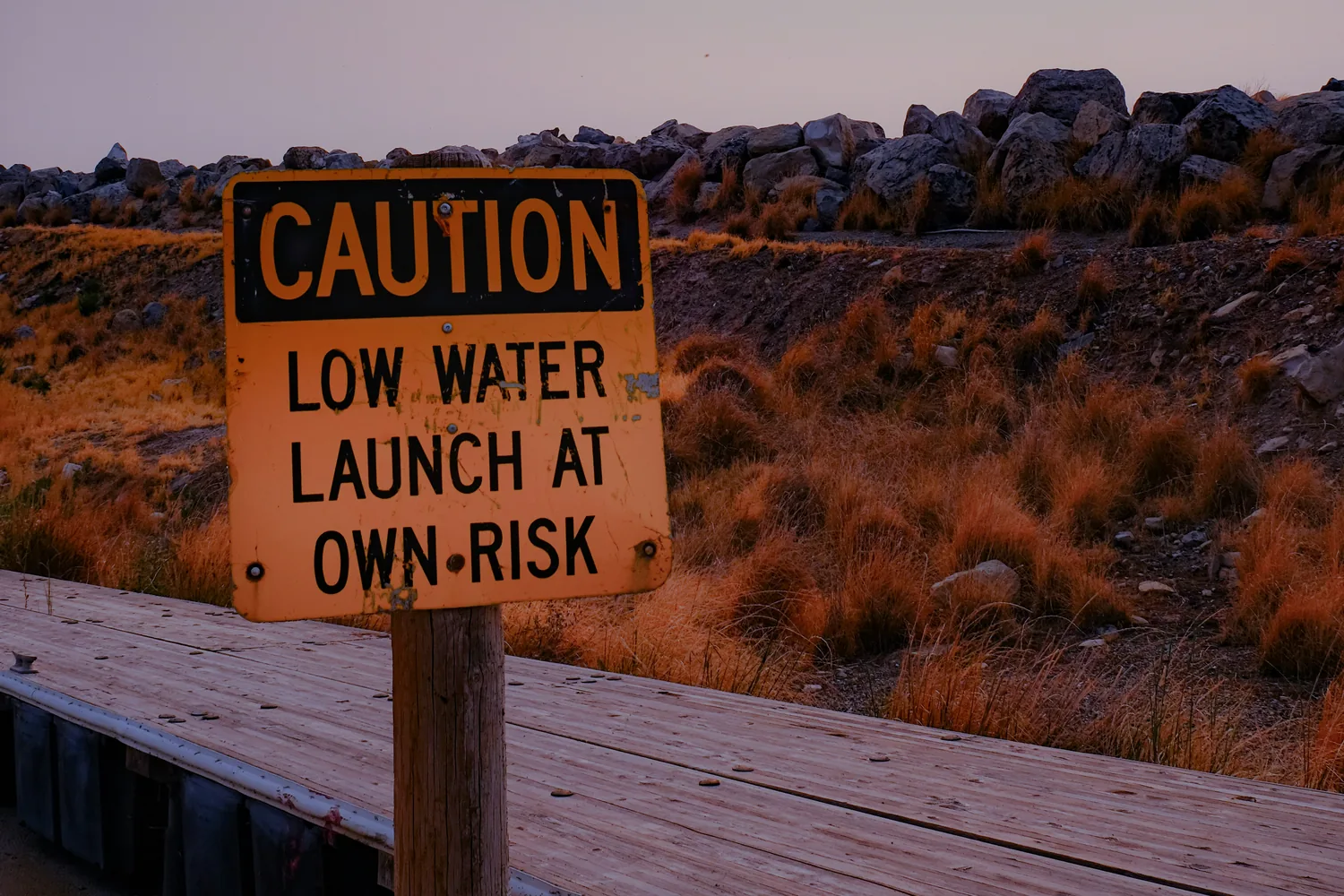 A CAUTION: LOW WATER sign on a wooden launch dock at dusk
